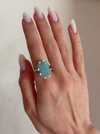 Hand wearing a ring with a blue gemstone on a neutral background