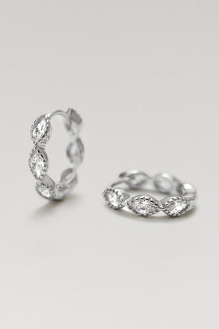 A pair of silver huggie hoop rings with marquise-cut stones, displayed on a clean light gray background.