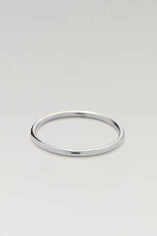 A minimalist polished silver bangle bracelet with a smooth, rounded profile, displayed on a neutral light gray background.