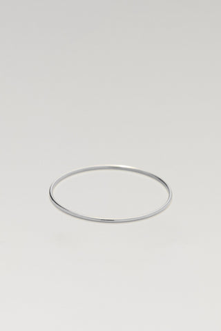 A minimalist, thin silver metal bangle bracelet centered on a light gray gradient background.