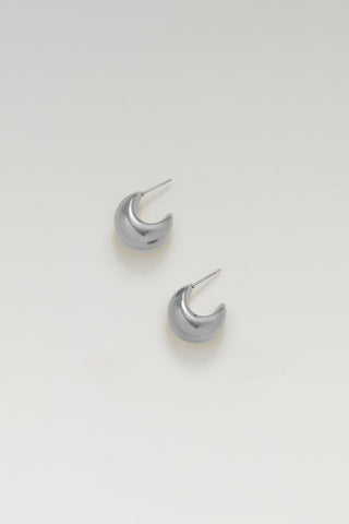 A pair of small silver crescent moon stud earrings on a clean, light gray background.