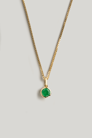 A gold chain necklace with a small round bezel-set green gemstone pendant, displayed against a neutral light gray background.