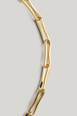 A close-up of a gold paperclip chain necklace against a solid light gray background.
