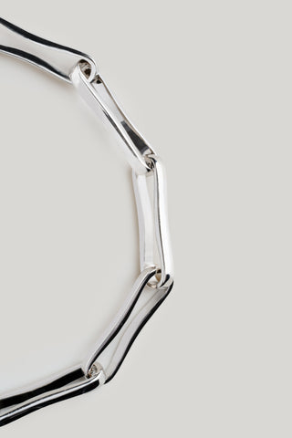 A close-up of a polished silver geometric link bracelet on a light gray background.