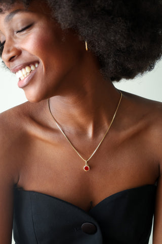 A gold chain necklace with a small oval red gemstone pendant, shown around a models neck