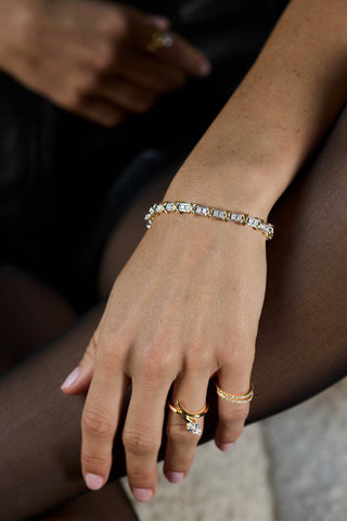 Two-tone Renata bracelet on the wrist, hand resting on the knee with a pear-shaped stone ring and a pave band
