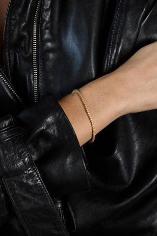 Alma mini tennis bracelet, gold plated, worn on the wrist over a black leather jacket