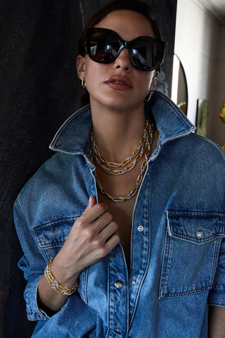 Model in sunglasses and a denim shirt wearing three layered two-tone Allegra necklaces and a stack of Allegra bracelets