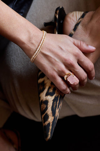 Gold plated Nico and Clara tennis bracelets stacked on the wrist, hand on a leopard-print heel with a pink stone ring