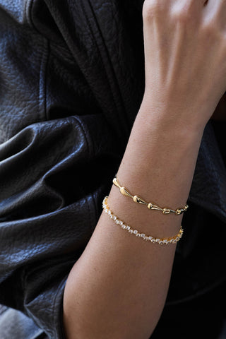 Riva bracelet and Ramona tennis bracelet, both gold plated, stacked on the wrist over a black leather jacket