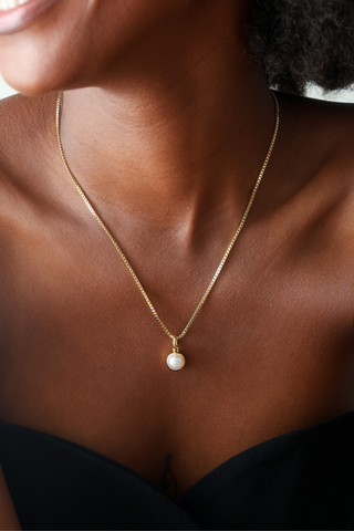 A close-up of a model wearing a delicate gold chain necklace with a single white pearl pendant.